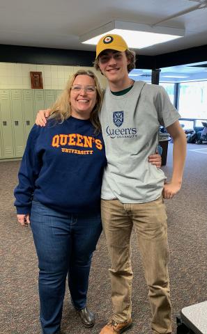 Julie Smith, wearing a Queen's sweatshirt, has her arm around Graeme Jagger, who also wears a Queen's t-shirt. Behind them is a set of lockers.
