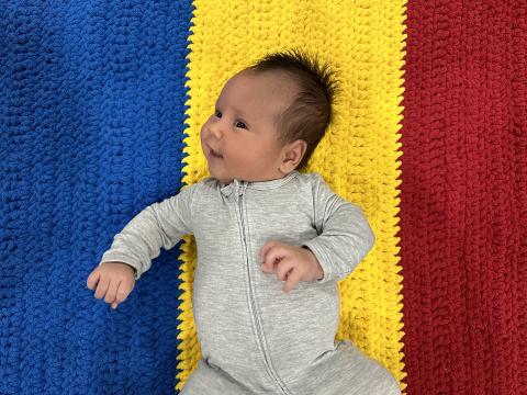 A baby lies on a tricolour knitted blanket.