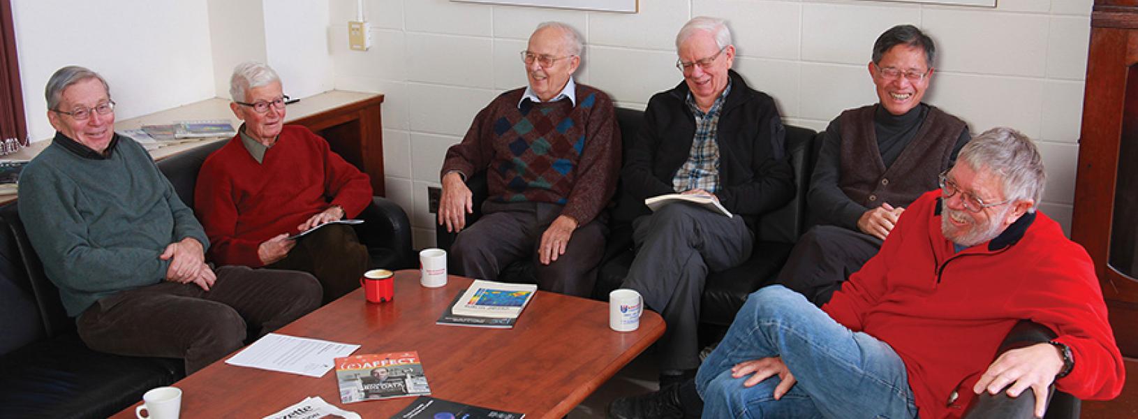 From left to right: Barry Robertson, Hugh Evans, George Ewan, Hamish Leslie, Hay Boon Mak and Peter Skensved, sitting around a table, laughing.