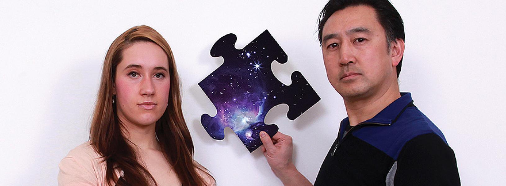 Jennifer Mauel and Mark Chen, holding a puzzle piece with a solar system image on it, posing for the camera.