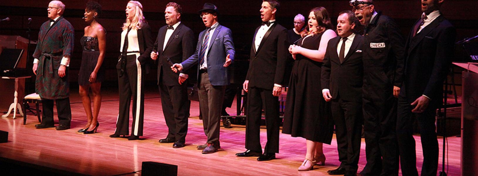 A nicely dressed group of people, singing, on stage at the Isabel