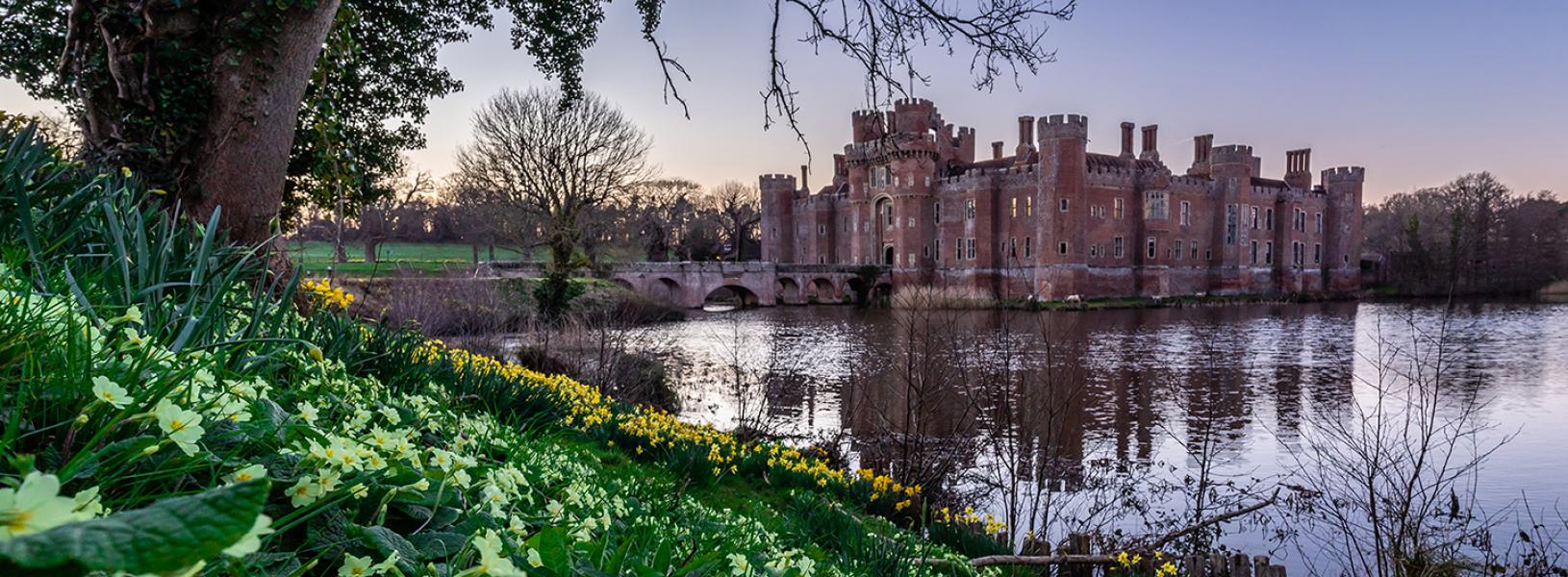 Herstmonceux Castle is the background and blooming daffodils in the foreground that is separated by a pond