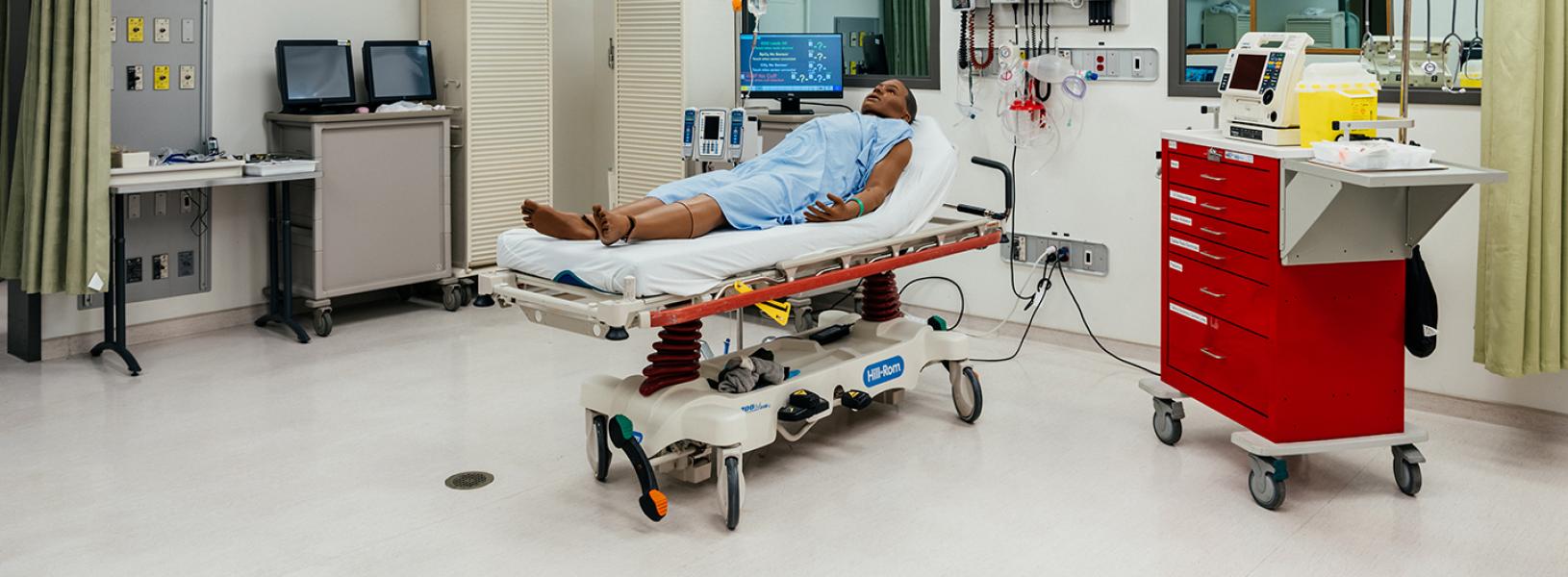 Wide view of a hospital room with the SimMan 3G Plus lying on a gurney in the middle of the room.