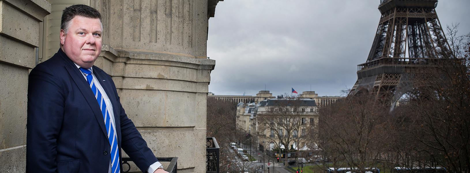 Andrzej Antoszkiewicz stands on a balcony that overlooks the Eiffel Tower.