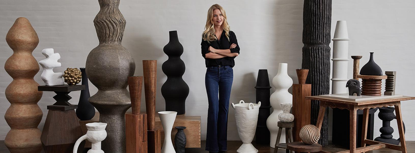 Christiane Lemieux standing with her arms crossed among very tall vases and objects d'art from her product collection.