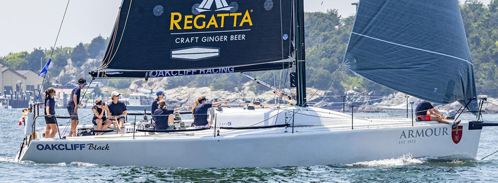 Members of the Oakcliff Black sailboat crew sit on the deck. The marina is in the background.