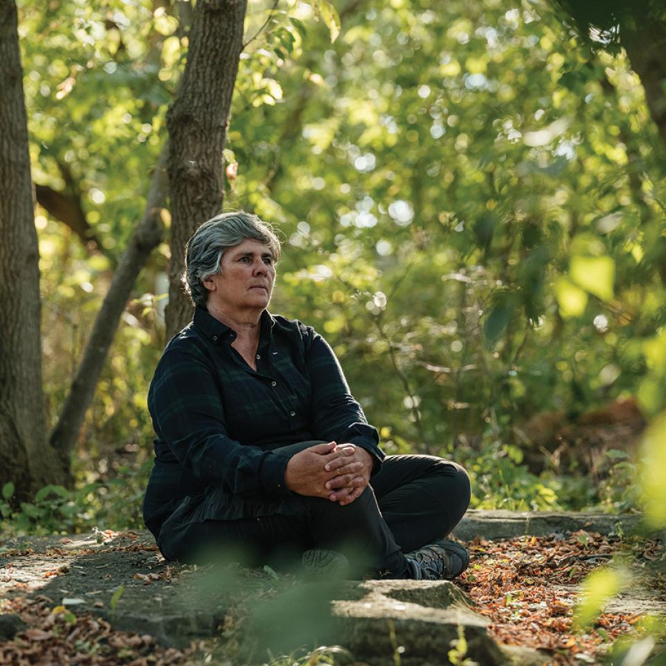 Woman sitting cross legged on the ground in the woods.