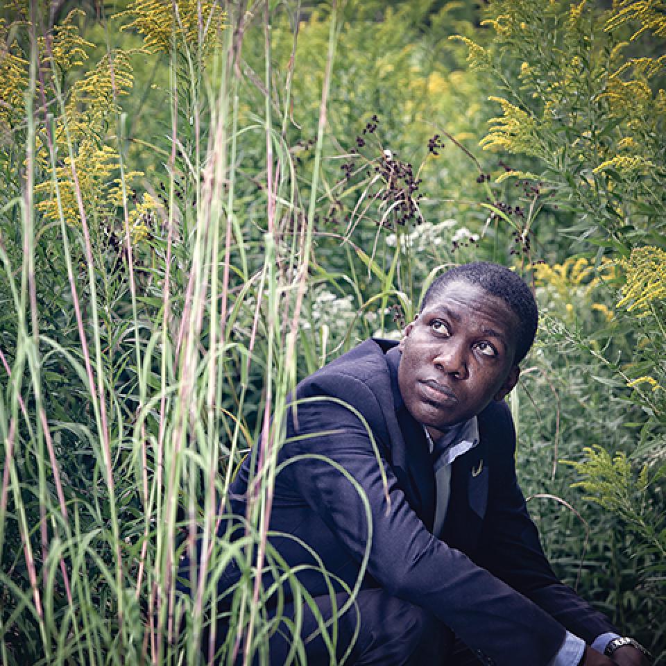 Oluwatobiloba (Tobi) Moody crouching in grass and looking up.