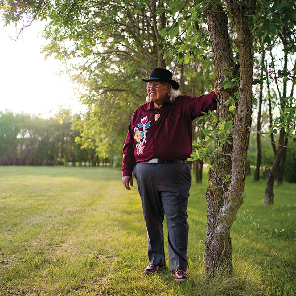 Murray Sinclair standing in the woods with his hand leaning against a tree.