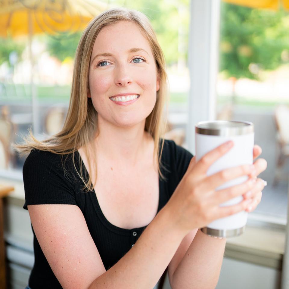 Tara McKenna sitting in a coffee shop, holding a beverage in a reusable mug.