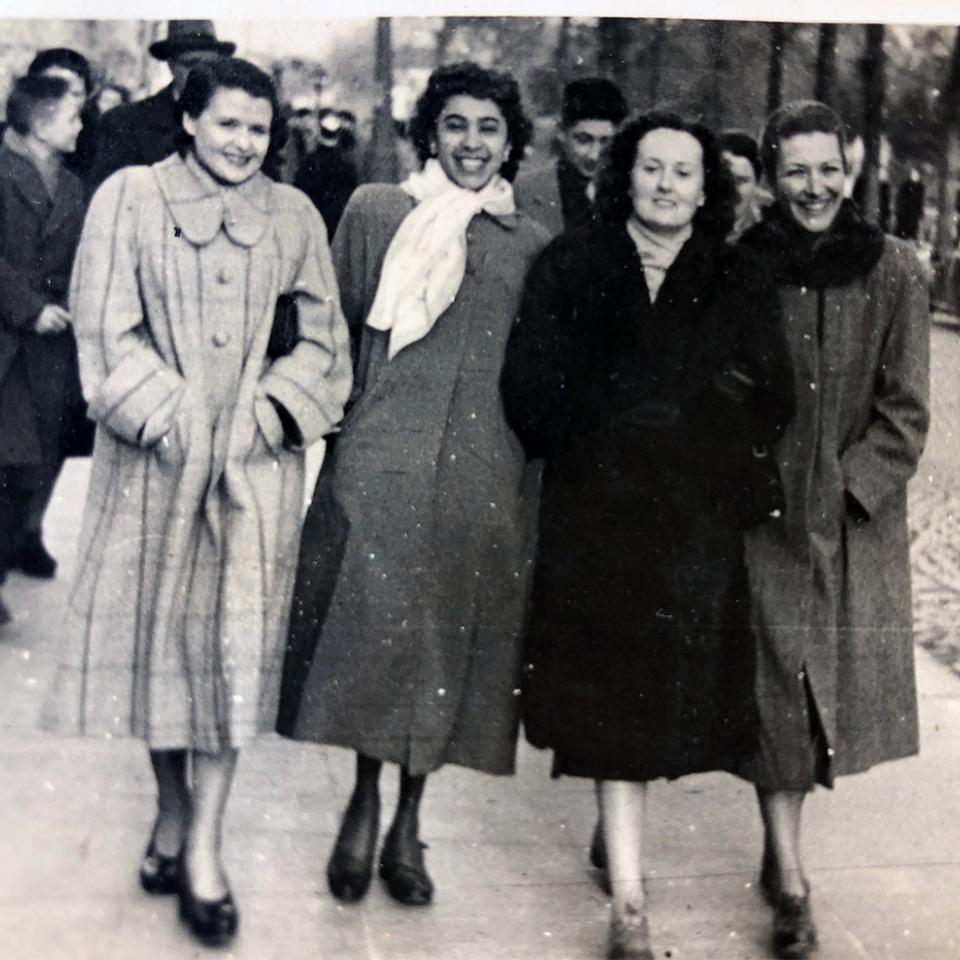 A old black and white stained photograph of Elizabeth Kawaley and three friends. They are wearing winter coats and walking towards the camera.