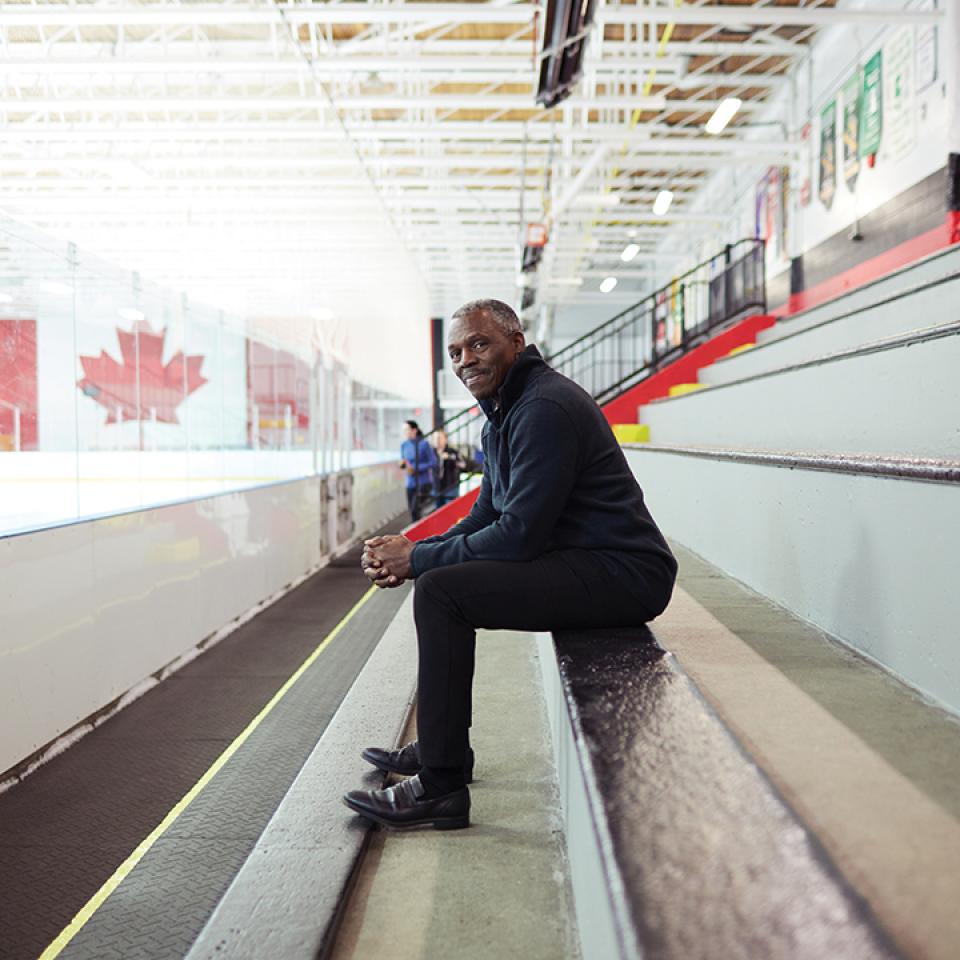 Hugh Fraser sits in the bleachers at a hockey rink.