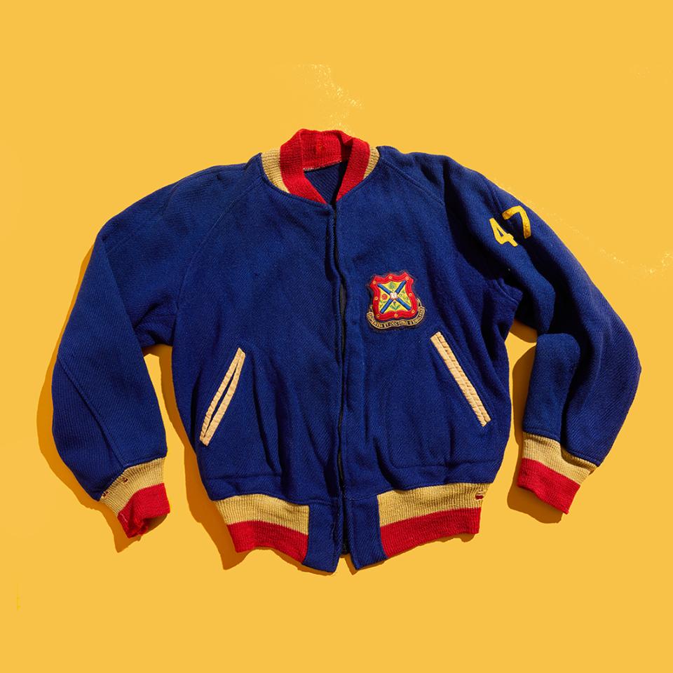 The front of a wool-and-knit Queen's jacket, with 47 on the sleeve, lies flat on a yellow background.