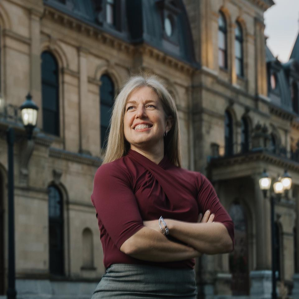 Susan Holt stands with her arms crossed in front of a historic building.