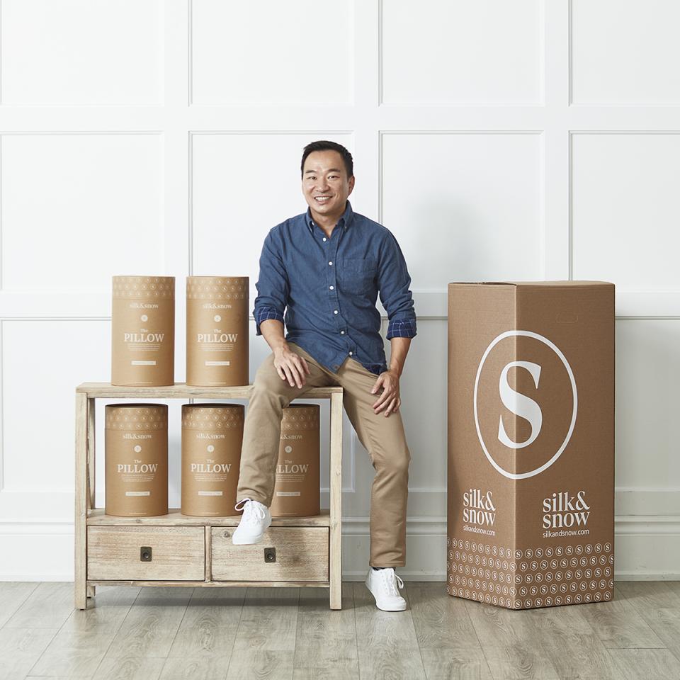 Albert Chow sits with one leg on a table. There are silk & snow boxes around him.