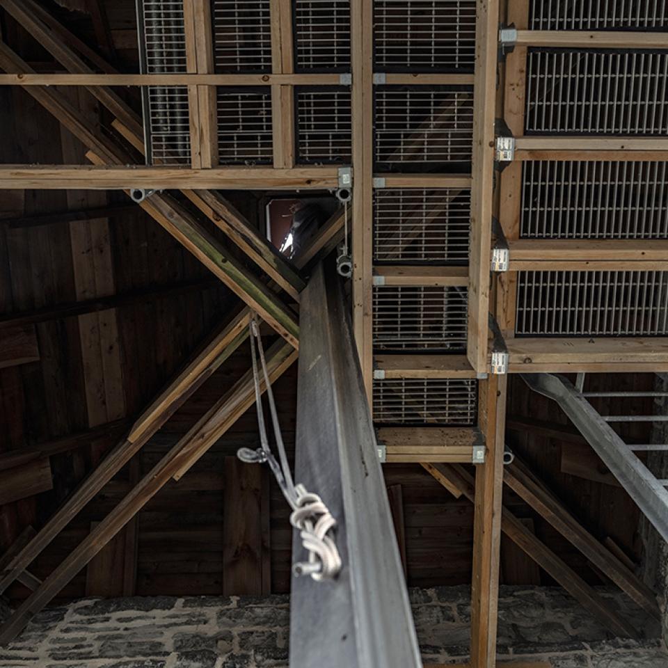View upward inside the clock tower showing wooden beams, metal supports, and a vertical drive shaft.