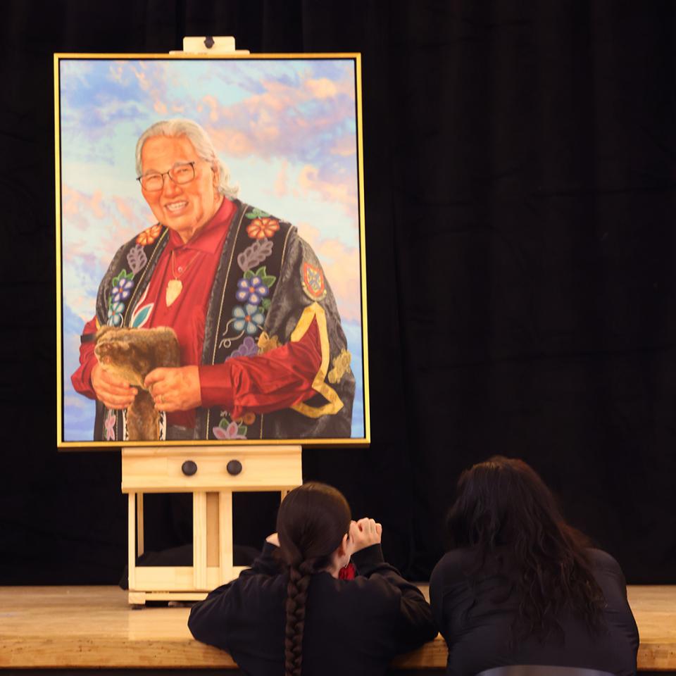 Two attendees look up at a large framed portrait on an easel during a portrait unveiling ceremony.