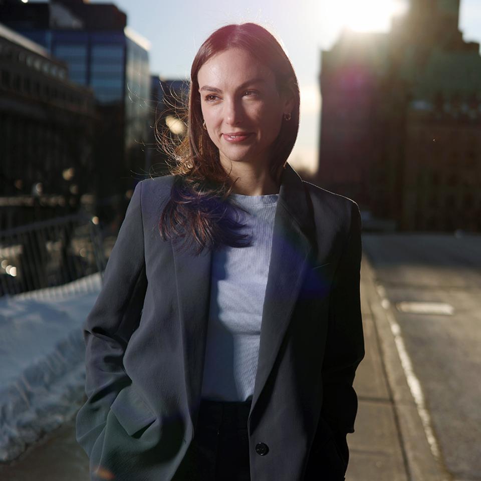 Portrait of a woman in business attire standing outdoors on a city street with sunlight behind her.
