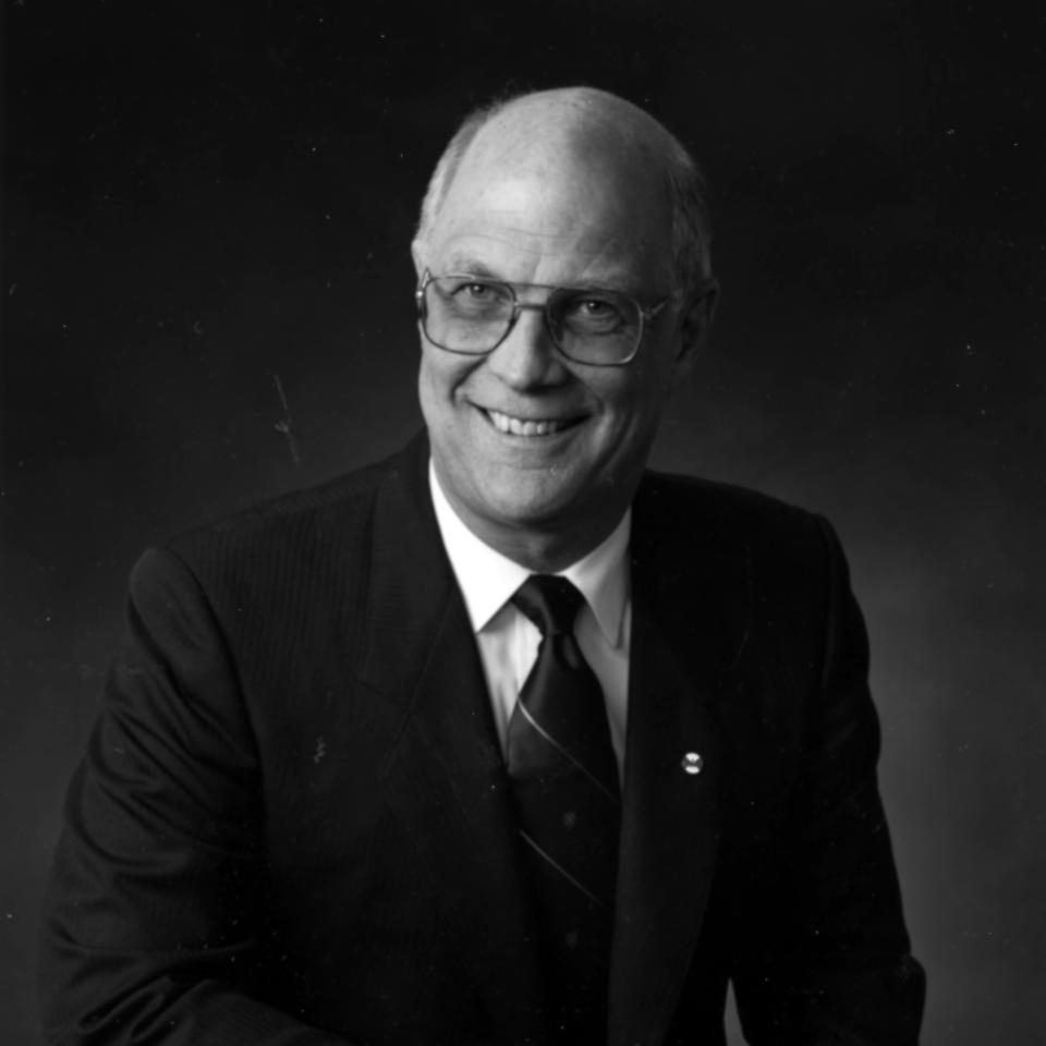 Black-and-white portrait of a smiling man in glasses, a suit, and tie.