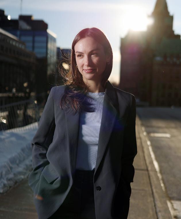 Portrait of a woman in business attire standing outdoors on a city street with sunlight behind her.