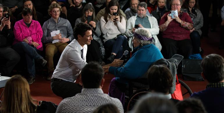 Prime Minister Justin Trudeau kneels on the floor to take a question from Laurel Claus-Johnson, who sits in a wheelchair, during a town hall in Kingston in January 2017.