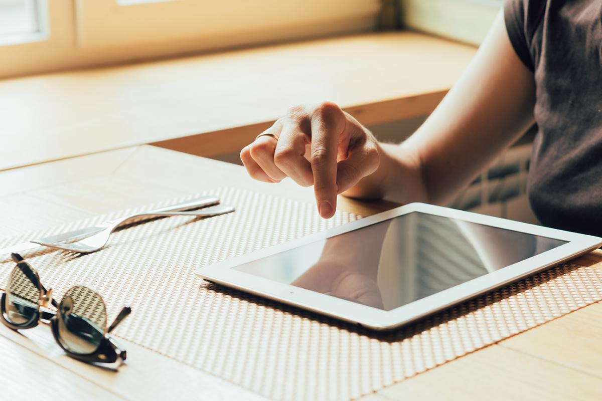 Photo of an iPad sitting on a table and a person's finger moving over the screen. 