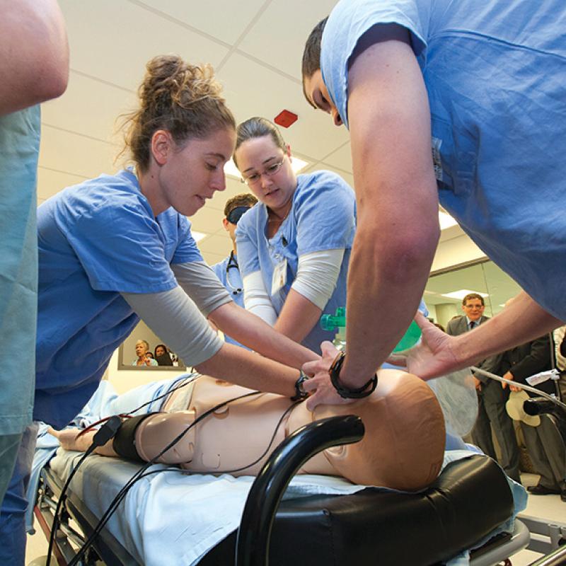 students in scrubs practicing medical procedure on a prop body