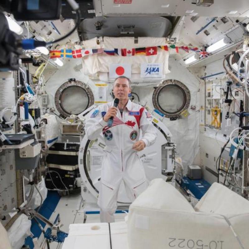Drew Feustel holding a microphone, answering questions from inside his spacecraft.
