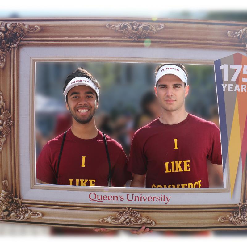 Two students standing behind a picture frame.