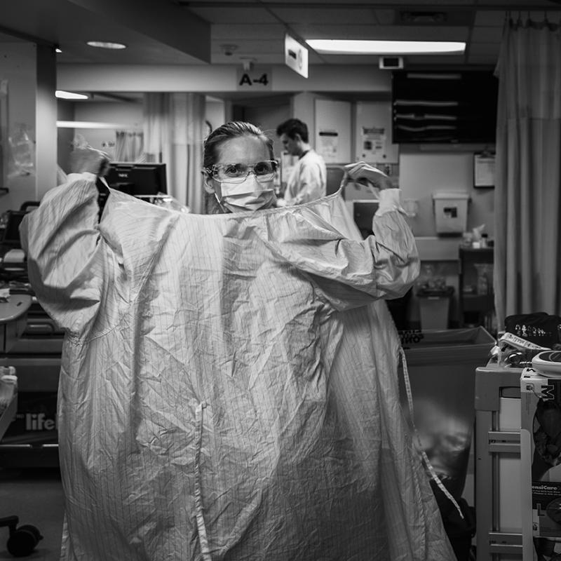 A medical worker looking at the camera putting her gown on.
