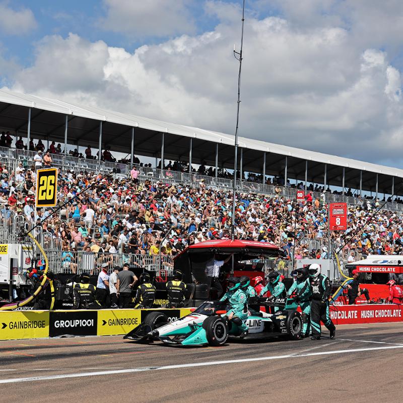 Race car in the pit with a crowd of bleachers behind 