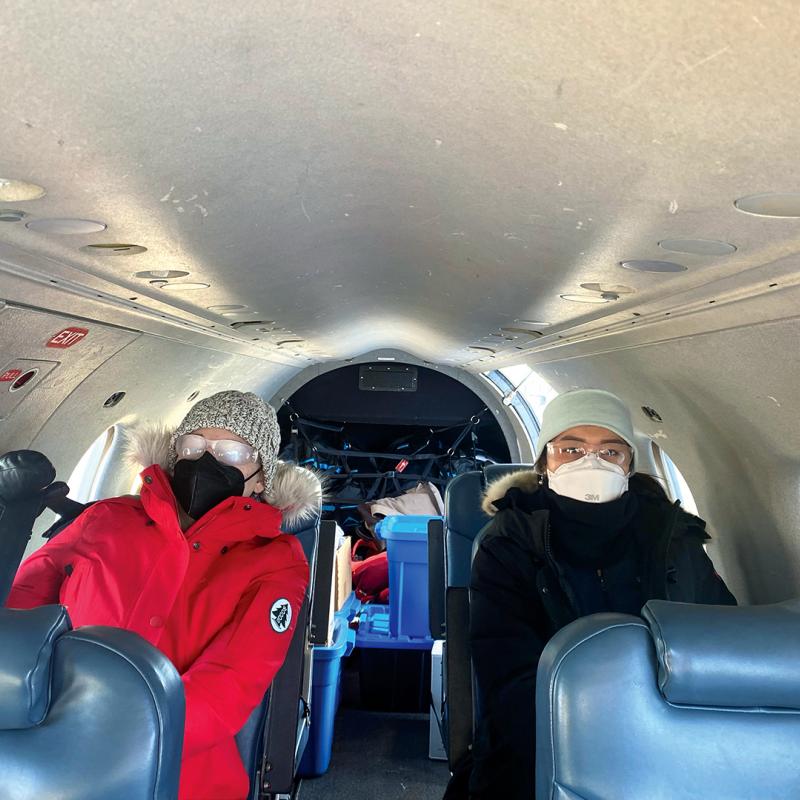 Two people dressed in winter coats, hats, and face masks, aboard a cargo plane