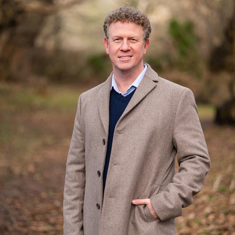 Dr. Simon Coppard standing in the woods wearing a tweed jacket with his hand in his pocket