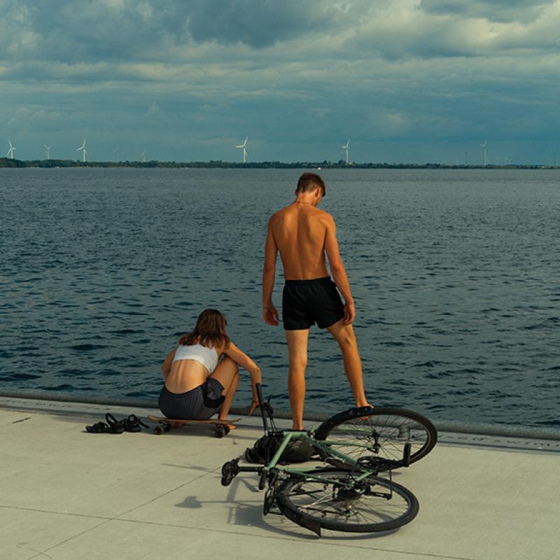 A male and female standing on a pier with Wolfe Island and the giant windmills in the distance.