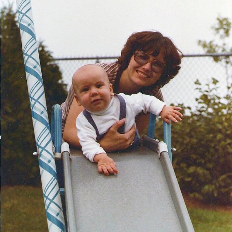 A woman holds a baby at the top of a kiddie slide