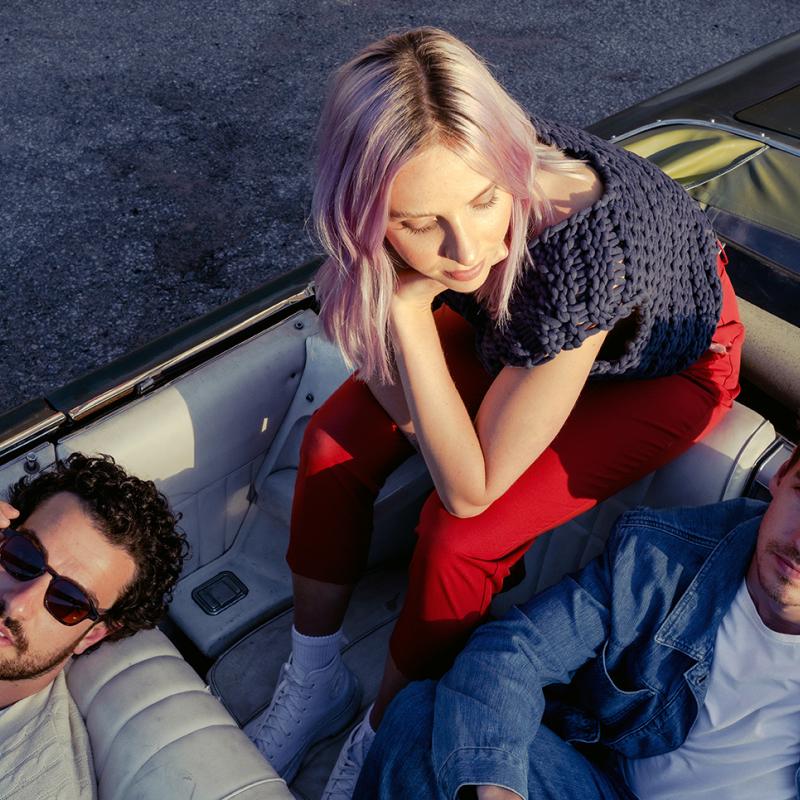 Two men and one woman sit in a convertible car, looking above at the camera.