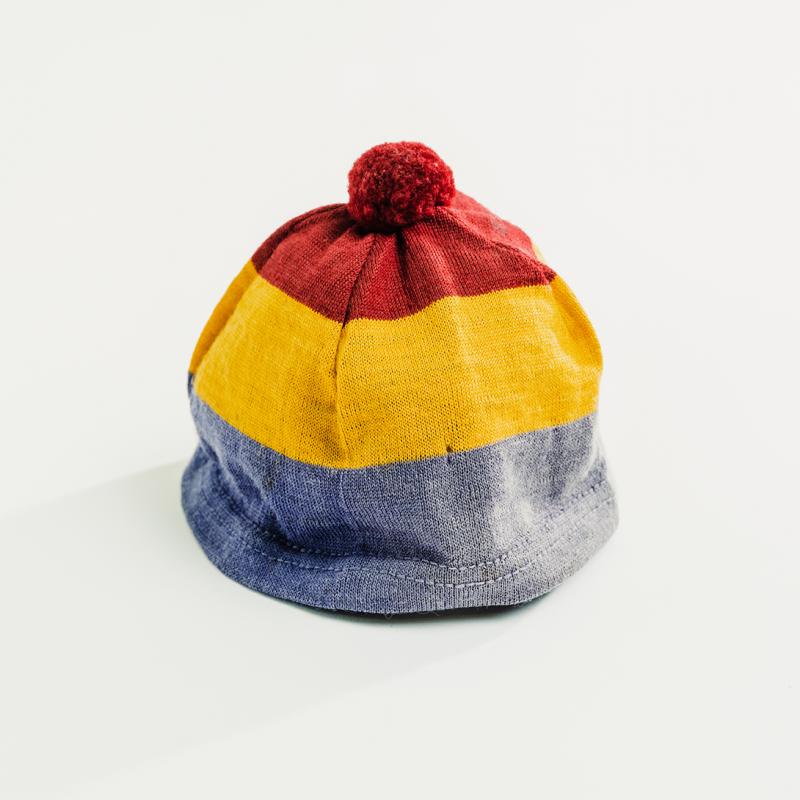 A striped toque with a pompom, in horizontal Queen's colours, sits upright.