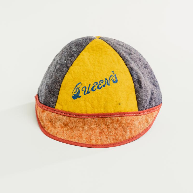A vintage Queen's beanie, in alternating vertical blue and yellow stripes, a red brim, and old Queen's lettering, sits upright.