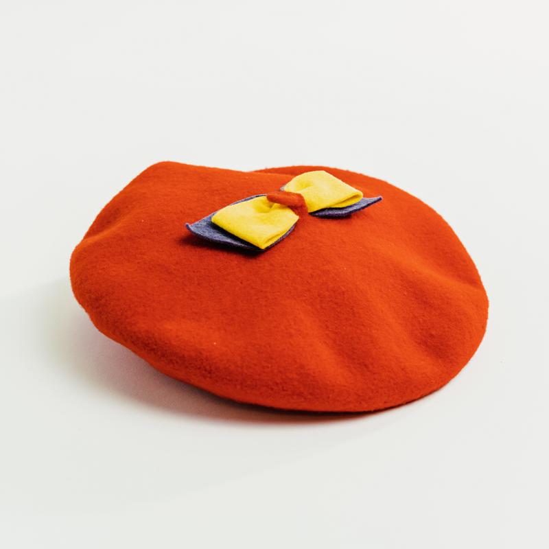 A vintage red Queen's beret, with a yellow and blue bow on top, sits upright.
