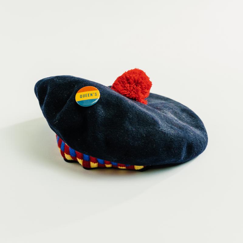 A traditional black Queen's tam, with a red pompom on top and tricolour checkered band, sits upright.