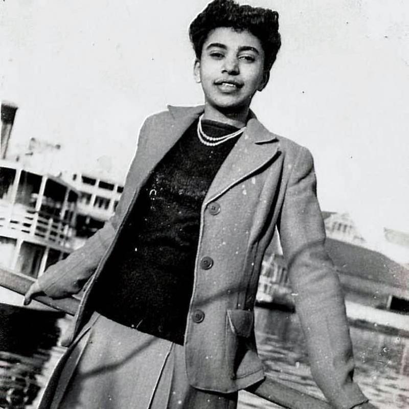 An old black and white photo of Elizabeth Kawaley leaning against a railing by the waterfront. 