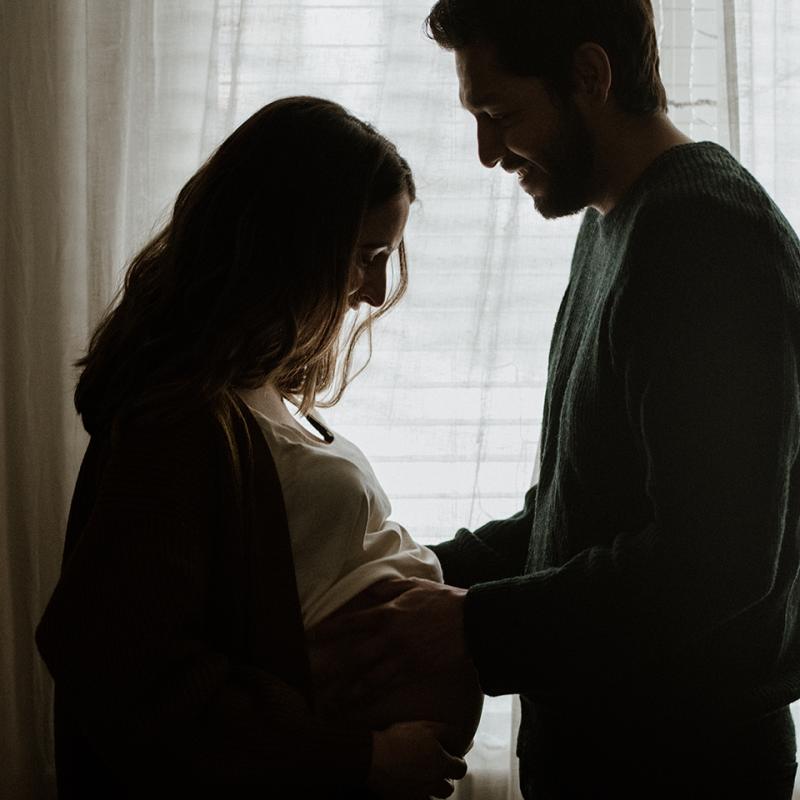 Pregnant couple in silhouette. Husband's hands rest on pregnant belly.