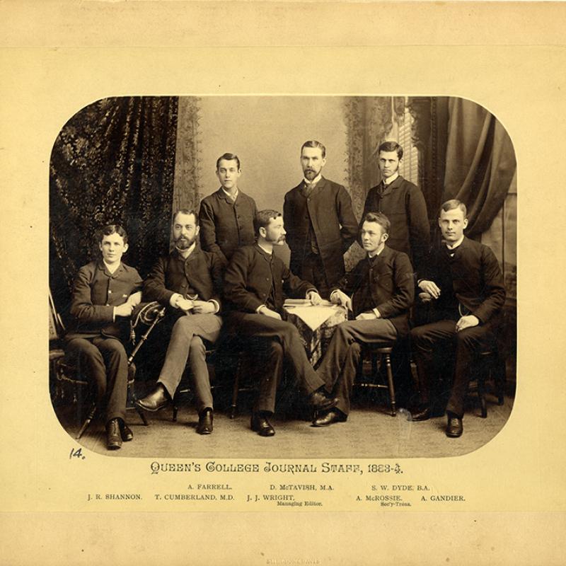 Queen's College Journal staff in 1884. Eight men pose in front of drapes.