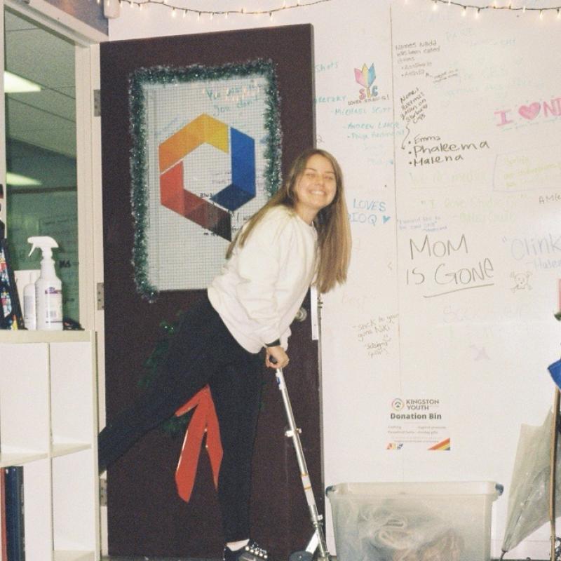 Niki Boytchuk-Halesmiling and posing on a scooter inside Studio Q, with walls covered in drawings and messages from students.
