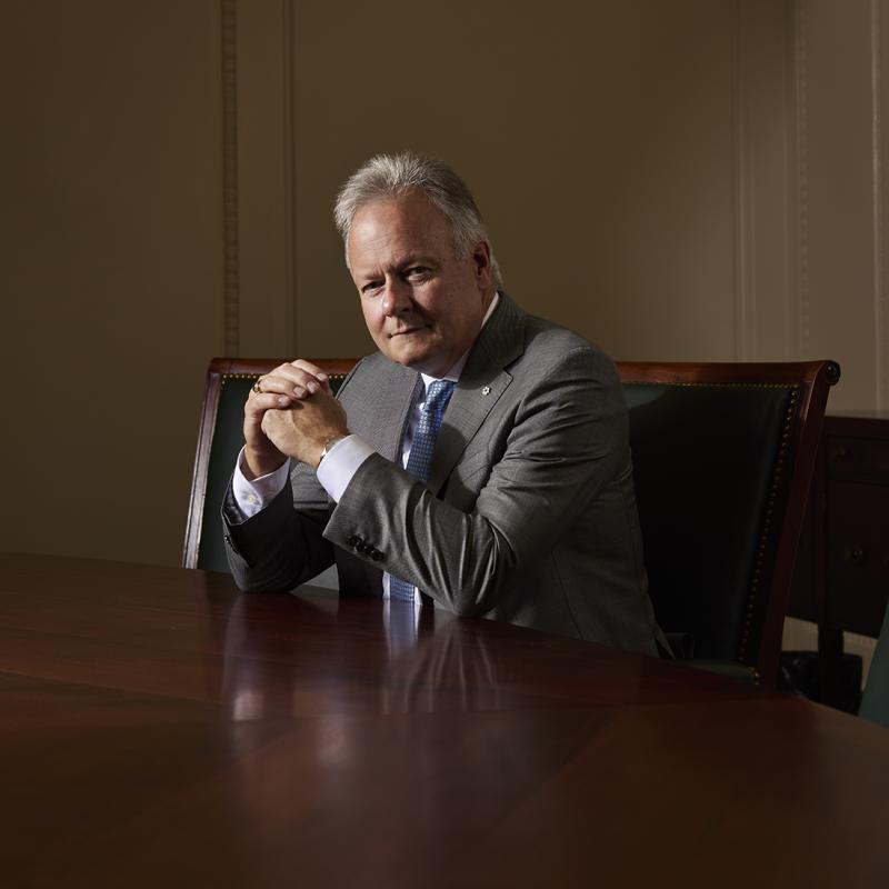 Portrait of Stephen Poloz seated at a boardroom table, wearing a gray suit and light blue tie.
