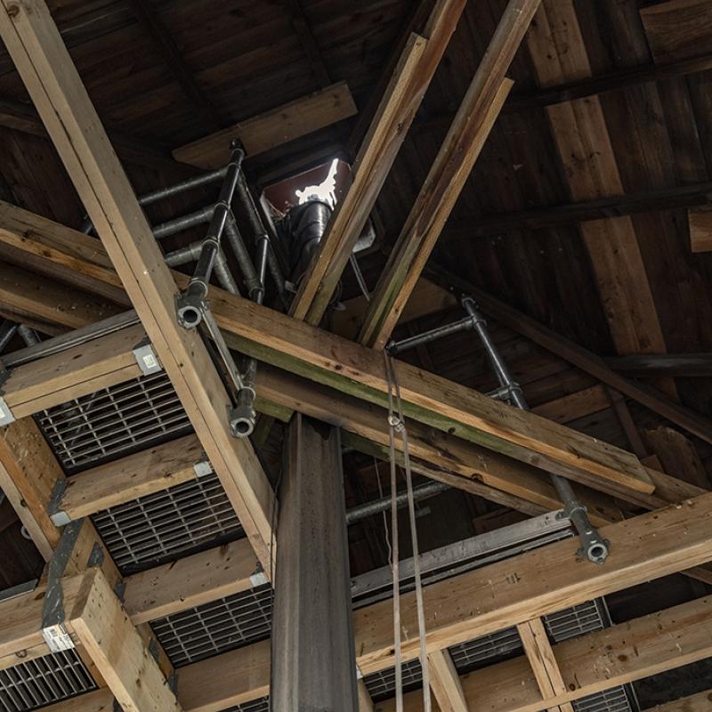 Interior view of timber framing and metal supports surrounding the clock tower’s central shaft.