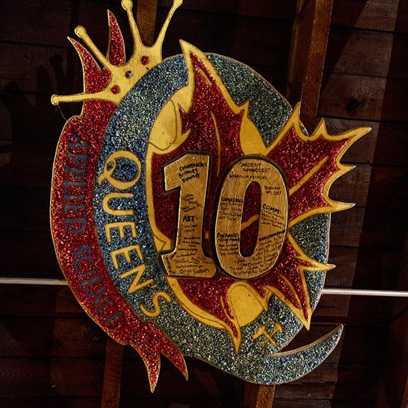 Colourful “Queen’s Science ’10” sign with signatures displayed against wood paneling.