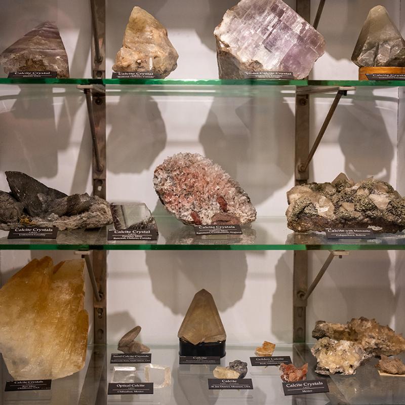 Glass display shelves holding labeled mineral and crystal specimens in a museum exhibit.