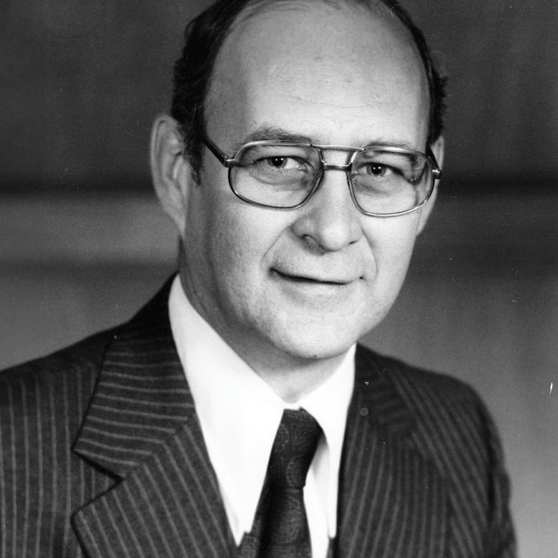 Black-and-white formal portrait of Duncan Sinclair wearing glasses and a pinstripe suit.