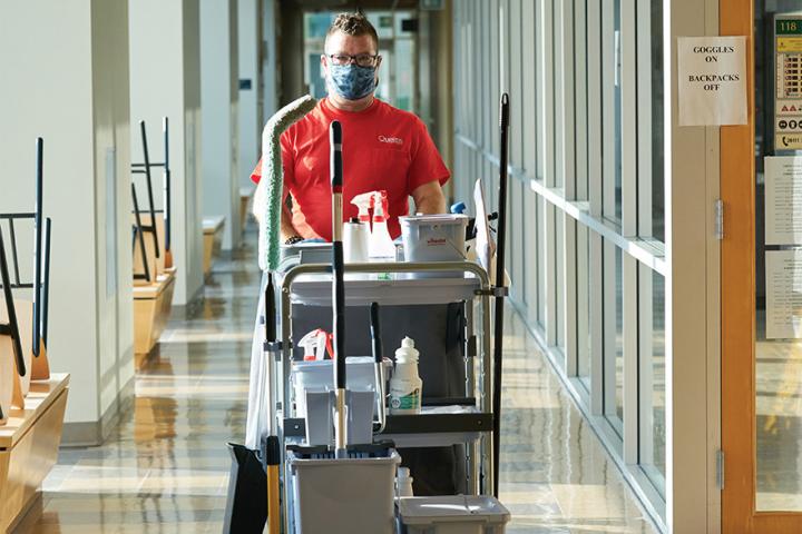 Facility services worker pushes a cart through Chernoff Hall while wearing a medical mask.
